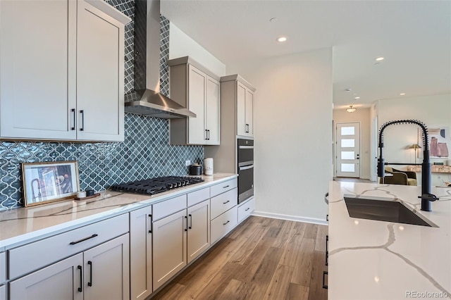 kitchen featuring wall chimney exhaust hood, sink, gas stovetop, light stone counters, and light hardwood / wood-style flooring