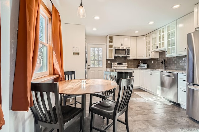 kitchen with appliances with stainless steel finishes, tasteful backsplash, light stone counters, pendant lighting, and white cabinetry