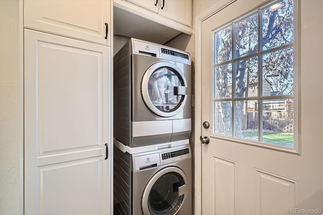 clothes washing area featuring cabinets, a wealth of natural light, and stacked washer and clothes dryer