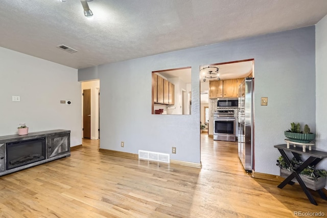 living room featuring light wood-type flooring, a textured ceiling, and baseboards