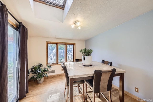 dining area featuring a skylight, healthy amount of natural light, light wood-style flooring, and baseboards