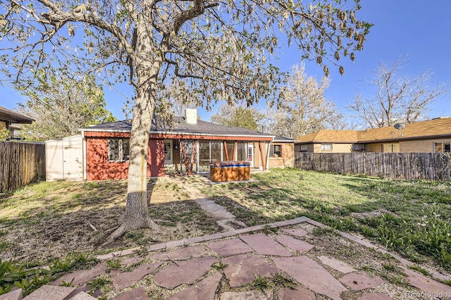 rear view of property featuring a hot tub, a patio, a shed, a chimney, and an outbuilding