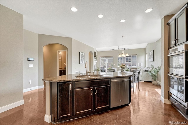 19382 Dunraven St, Parker, CO 80134 - kitchen with appliances with stainless steel finishes, arched walkways, open floor plan, a chandelier, and dark wood-style flooring
