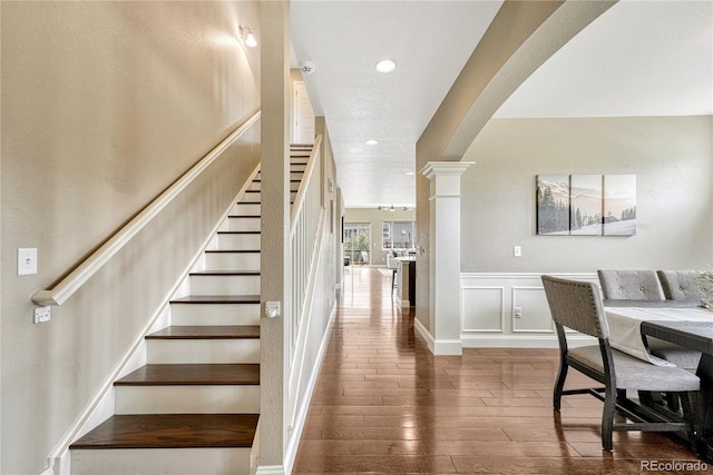 19382 Dunraven St, Parker, CO 80134 - stairway featuring arched walkways, wood finished floors, decorative columns, a wainscoted wall, and recessed lighting