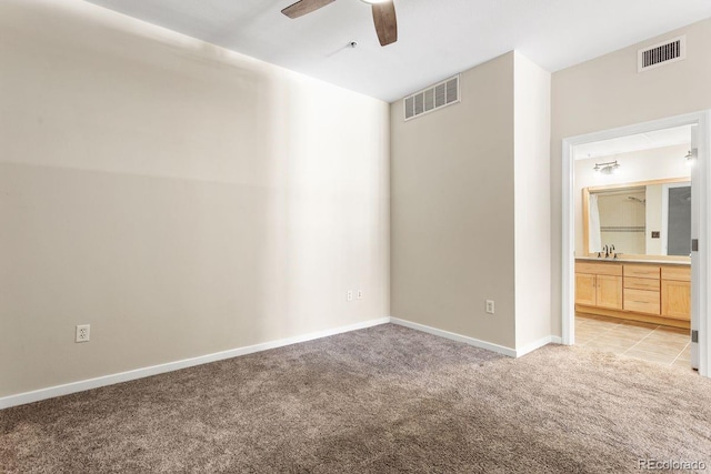 unfurnished bedroom featuring light carpet, a sink, baseboards, ensuite bathroom, and ceiling fan