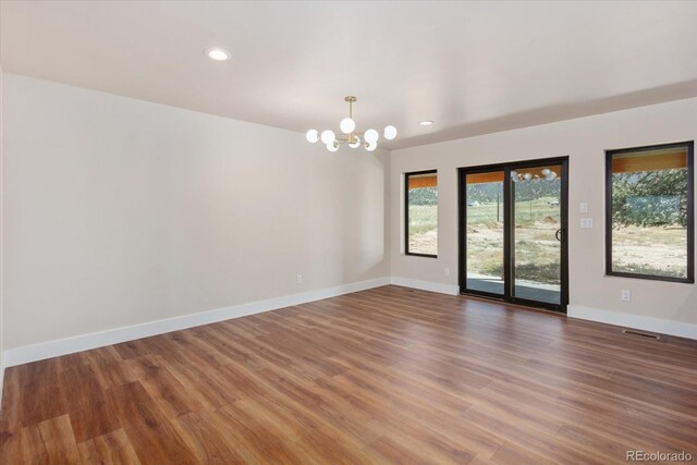 empty room featuring wood-type flooring and a notable chandelier