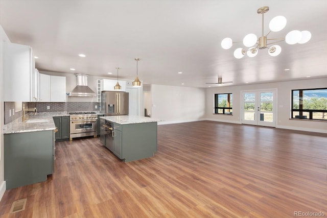 kitchen with appliances with stainless steel finishes, wall chimney exhaust hood, decorative light fixtures, white cabinets, and a center island