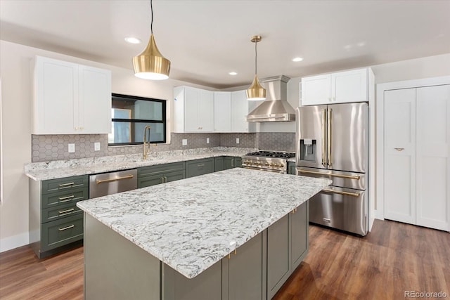 kitchen with a center island, high quality appliances, wall chimney exhaust hood, decorative light fixtures, and white cabinetry