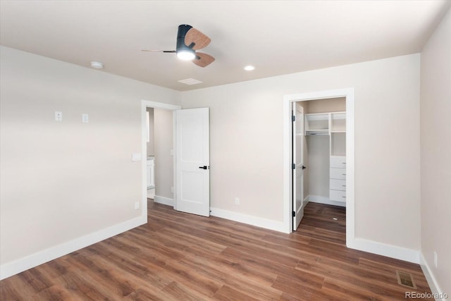 unfurnished bedroom with ceiling fan, a walk in closet, dark wood-type flooring, and a closet