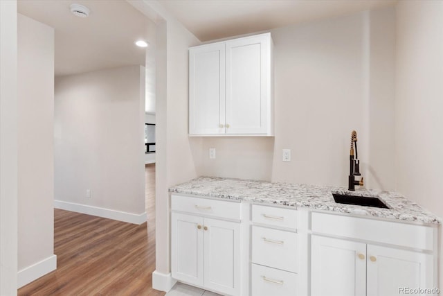 kitchen with light stone countertops, sink, white cabinets, and light wood-type flooring