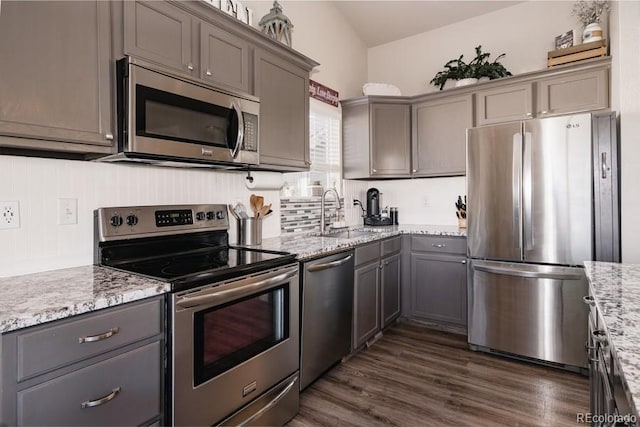 kitchen featuring stainless steel appliances, sink, light stone countertops, lofted ceiling, and dark wood-type flooring