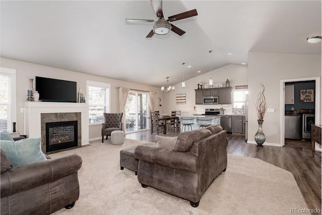 living room featuring hardwood / wood-style floors, ceiling fan with notable chandelier, a tiled fireplace, and lofted ceiling