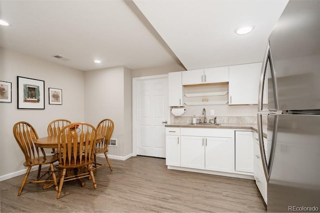 kitchen with sink, stainless steel fridge, light hardwood / wood-style floors, and white cabinetry