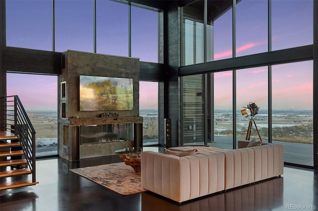 living room featuring stairway, a high ceiling, concrete flooring, a fireplace, and floor to ceiling windows