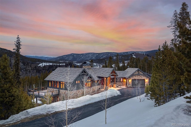 view of front of house with a garage, stone siding, a chimney, aphalt driveway, and a mountain view