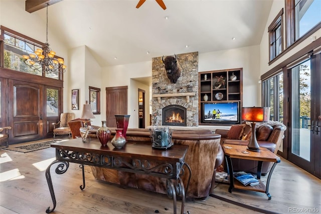 living area with high vaulted ceiling, a stone fireplace, a notable chandelier, wood finished floors, and french doors