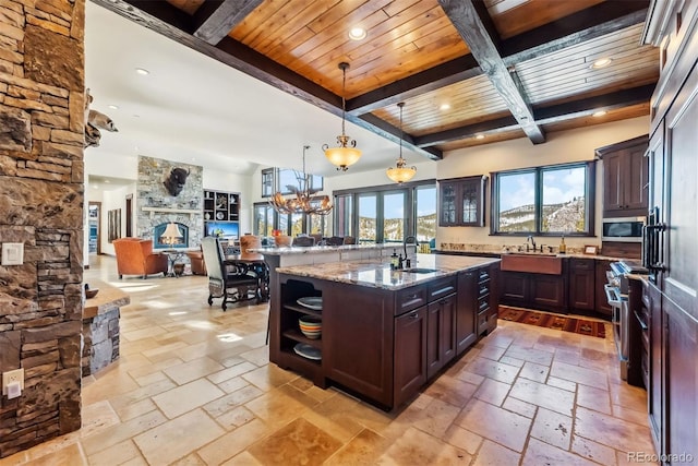 kitchen with stone tile floors, appliances with stainless steel finishes, a sink, a stone fireplace, and light stone countertops