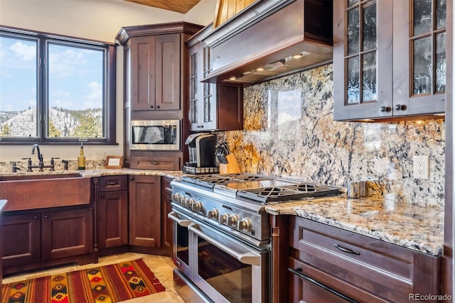 kitchen with light stone counters, appliances with stainless steel finishes, custom exhaust hood, decorative backsplash, and glass insert cabinets