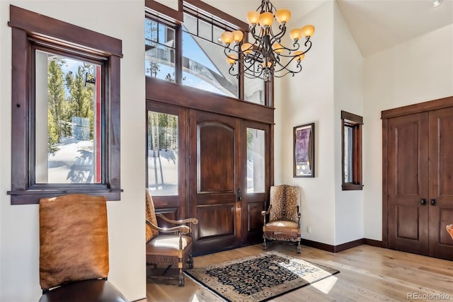 foyer featuring an inviting chandelier, light wood-style flooring, baseboards, and high vaulted ceiling