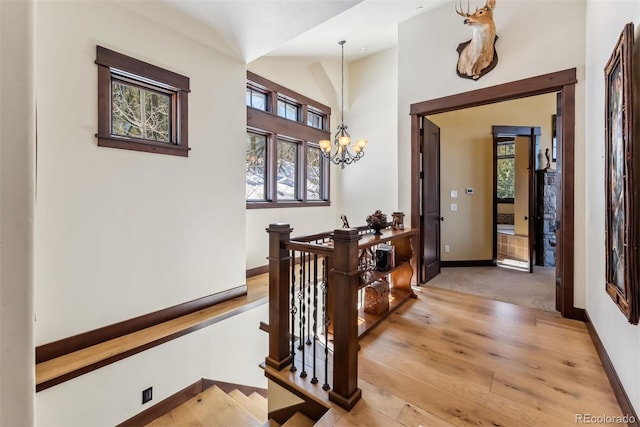 hallway featuring a notable chandelier, an upstairs landing, baseboards, vaulted ceiling, and light wood-style floors