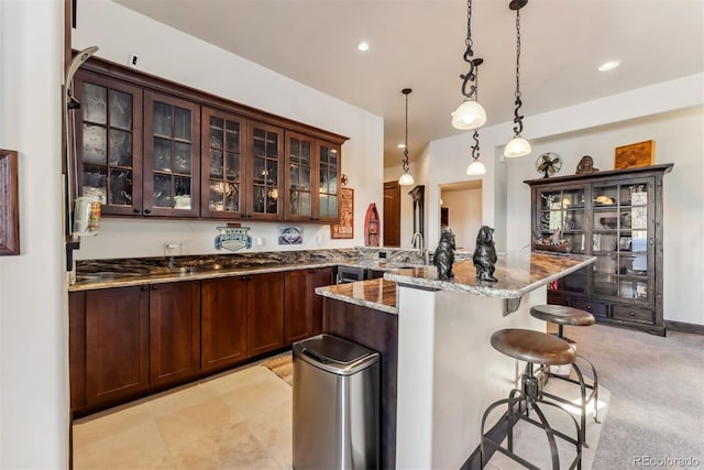 kitchen with light colored carpet, a breakfast bar, light stone countertops, glass insert cabinets, and pendant lighting