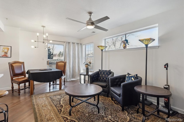 living area featuring visible vents, baseboards, wood finished floors, and ceiling fan with notable chandelier