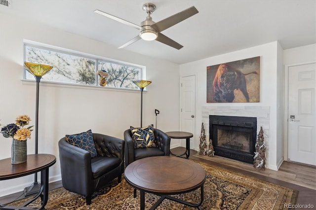 sitting room with ceiling fan, a fireplace, baseboards, and wood finished floors