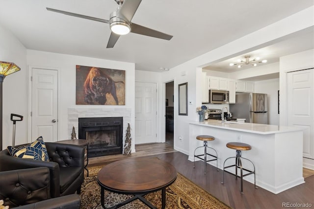 living area featuring dark wood-style flooring, a fireplace, a ceiling fan, and baseboards