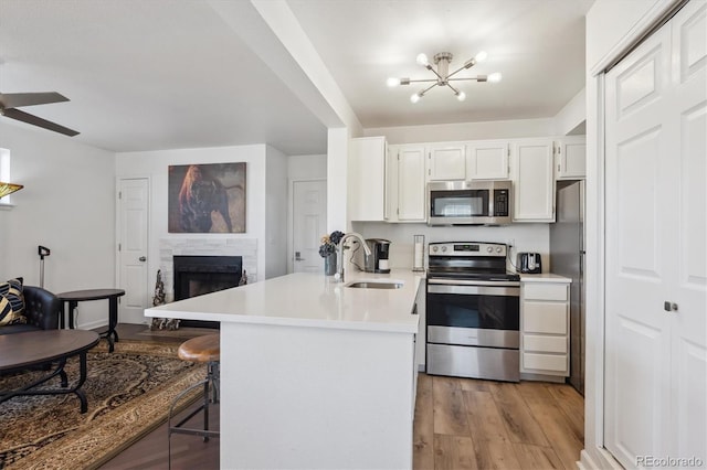 kitchen with stainless steel appliances, light countertops, a sink, light wood-type flooring, and a peninsula