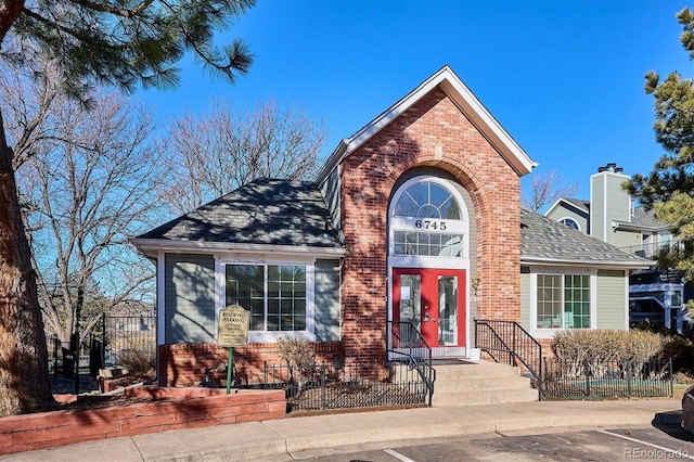 traditional home with french doors, brick siding, a shingled roof, and fence