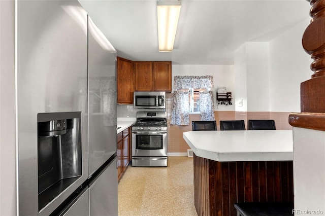 6981 Zuni St, Denver, CO 80221 - kitchen featuring brown cabinetry, a peninsula, light countertops, backsplash, and stainless steel appliances