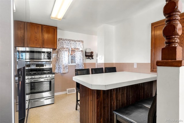6981 Zuni St, Denver, CO 80221 - kitchen featuring a peninsula, a breakfast bar, light countertops, brown cabinets, and stainless steel appliances