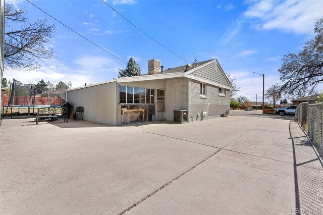 6981 Zuni St, Denver, CO 80221 - rear view of property featuring a trampoline, central AC unit, a patio area, brick siding, and fence