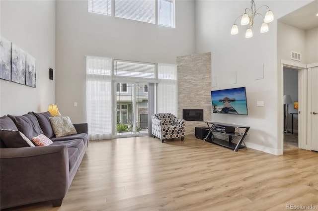 living room with a towering ceiling, a wealth of natural light, light hardwood / wood-style flooring, and a stone fireplace