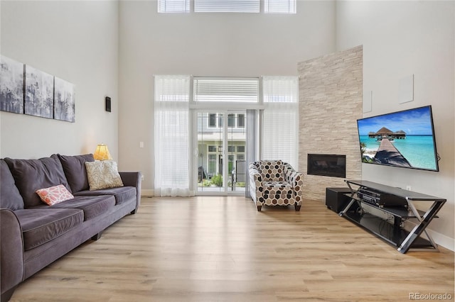 living room featuring a high ceiling, a stone fireplace, and light wood-type flooring