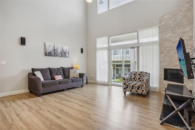 living room with wood-type flooring, a high ceiling, and a stone fireplace