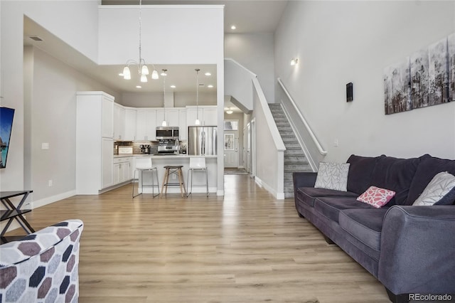 living room with a towering ceiling, an inviting chandelier, and light hardwood / wood-style floors