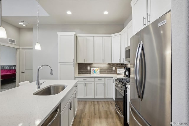 kitchen featuring hanging light fixtures, appliances with stainless steel finishes, sink, white cabinets, and light stone countertops