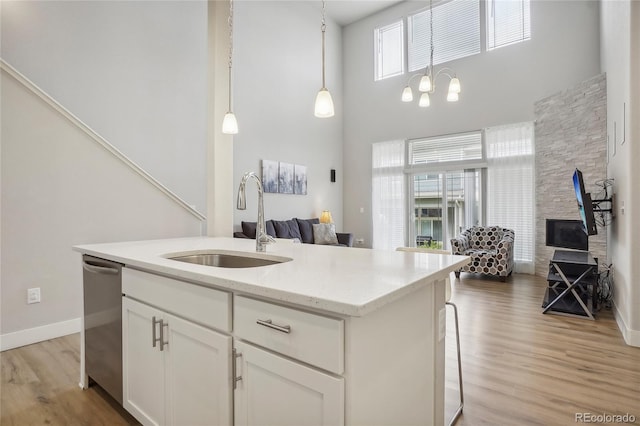 kitchen featuring hanging light fixtures, a kitchen island with sink, sink, white cabinets, and light stone counters