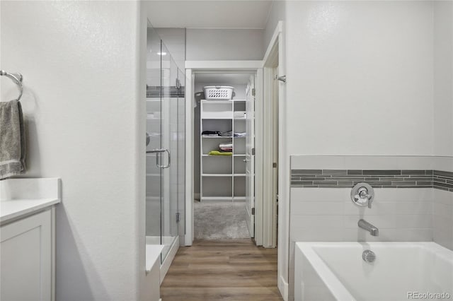 bathroom featuring wood-type flooring, vanity, and plus walk in shower