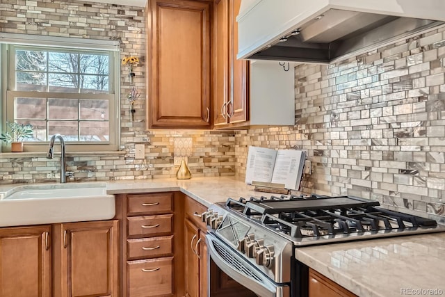 kitchen featuring sink, stainless steel range with gas stovetop, wall chimney range hood, light stone countertops, and backsplash