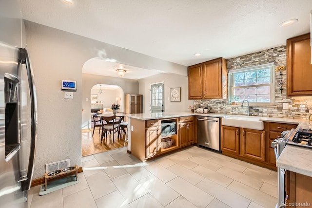 kitchen featuring sink, appliances with stainless steel finishes, backsplash, a textured ceiling, and kitchen peninsula