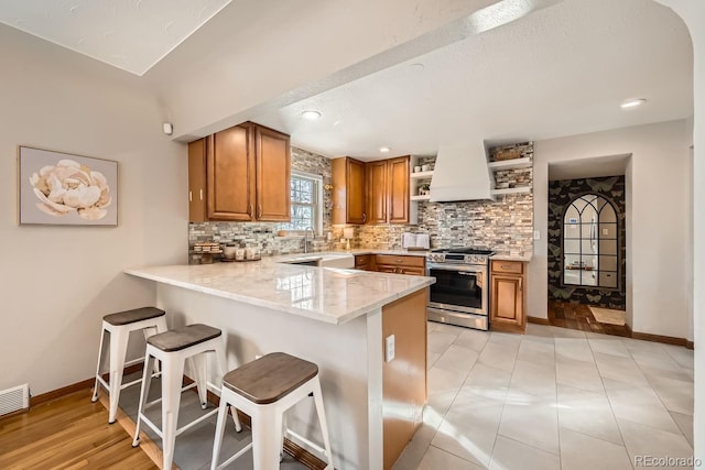 kitchen featuring gas stove, a breakfast bar area, kitchen peninsula, custom range hood, and decorative backsplash