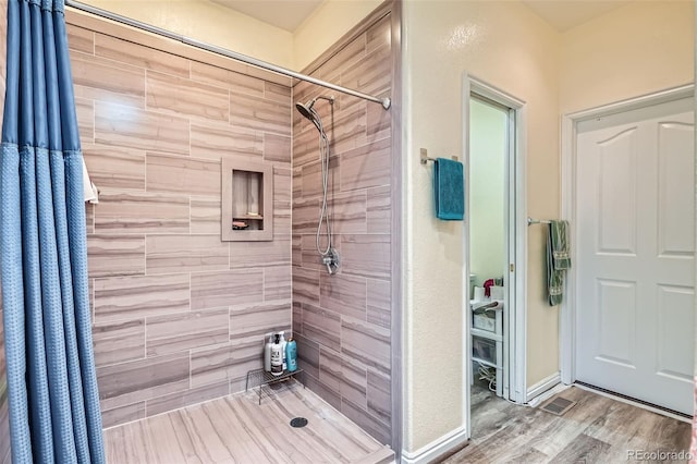 bathroom with baseboards, a tile shower, and wood finished floors