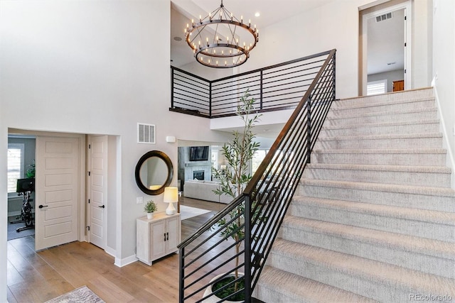 stairway featuring a high ceiling, wood-type flooring, and an inviting chandelier