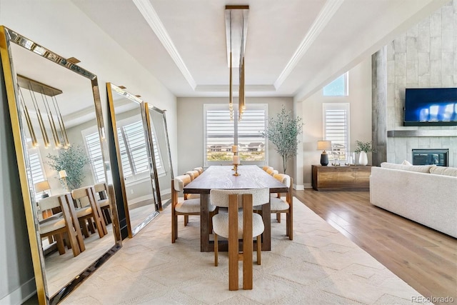 dining area with crown molding, a large fireplace, light hardwood / wood-style flooring, and a tray ceiling