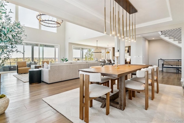 dining area with a notable chandelier, crown molding, light hardwood / wood-style flooring, and a raised ceiling