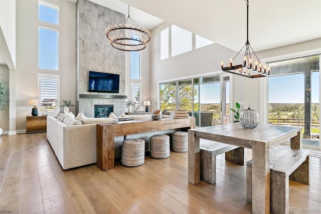 dining area featuring a towering ceiling, a notable chandelier, light wood-type flooring, and a fireplace