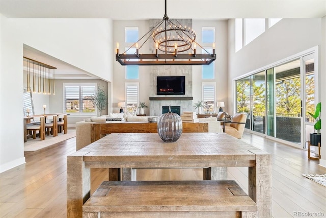 dining area with an inviting chandelier, hardwood / wood-style floors, a large fireplace, and a high ceiling