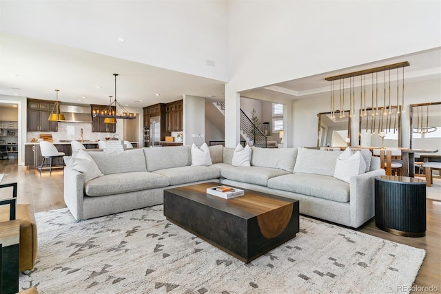 living room with crown molding, light hardwood / wood-style floors, a chandelier, and a high ceiling